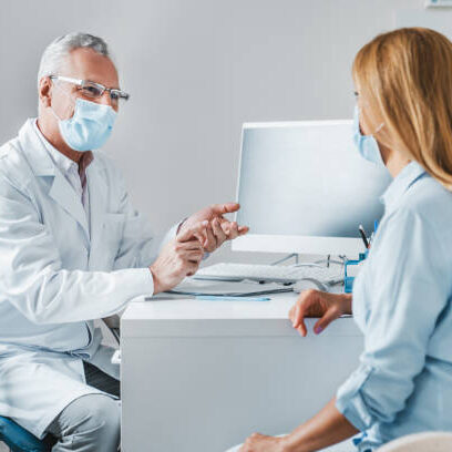 Senior male doctor wear protection face mask talking with patient in clinic office